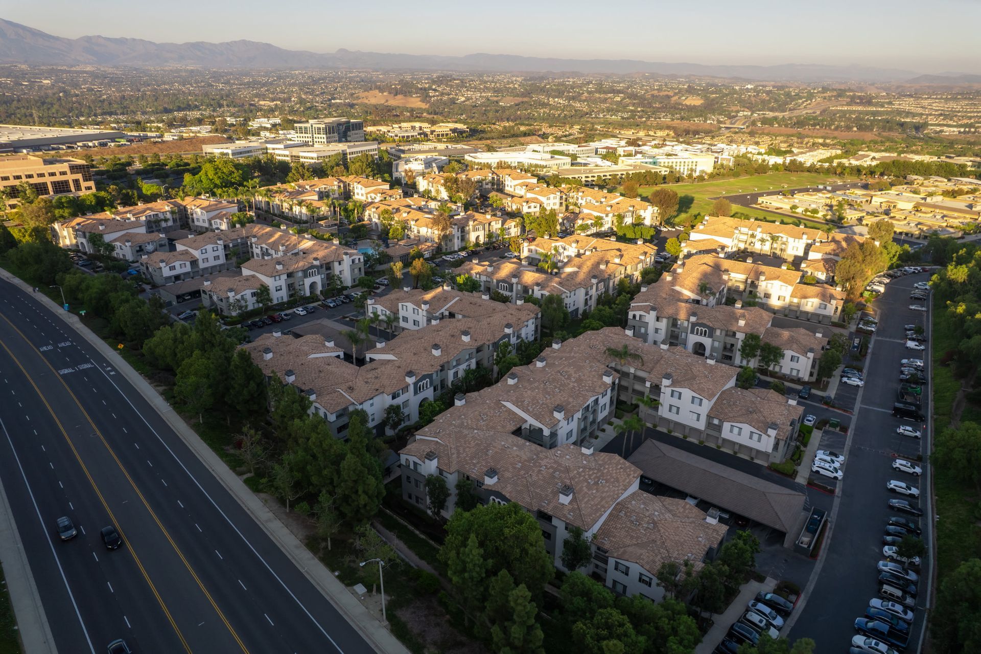 Aerial view of a large apartment community with tan roofs, roads, and surrounding greenery at Alize Apartment Homes in Aliso Viejo, CA.
