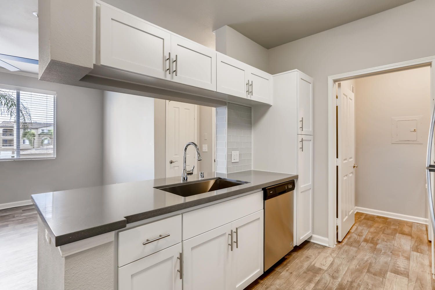Bright modern kitchen with white cabinets, gray countertops, stainless steel sink, and dishwasher at Alize Apartment Homes in Aliso Viejo, CA.