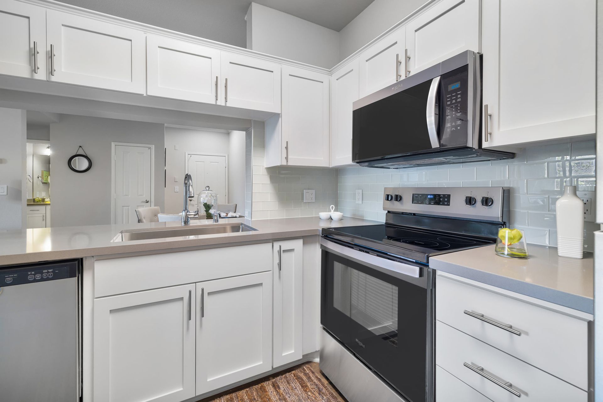 Modern white kitchen with island sink, stainless steel oven and microwave, and light gray countertops at Alize Apartment Homes in Aliso Viejo, CA.