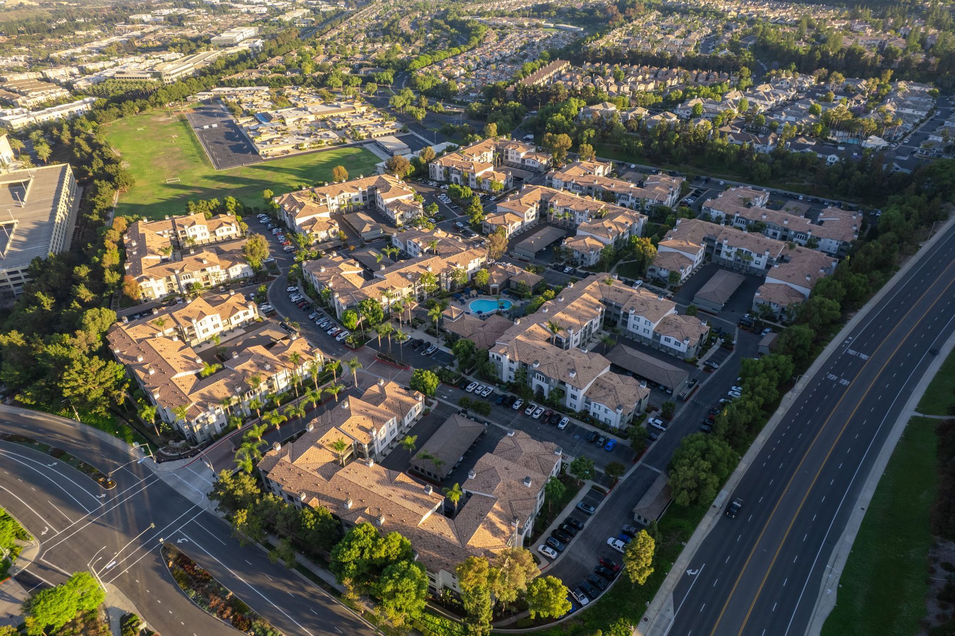 Aerial view of a large apartment community with multiple buildings, a central pool, and surrounding streets at Alize Apartment Homes in Aliso Viejo, CA.