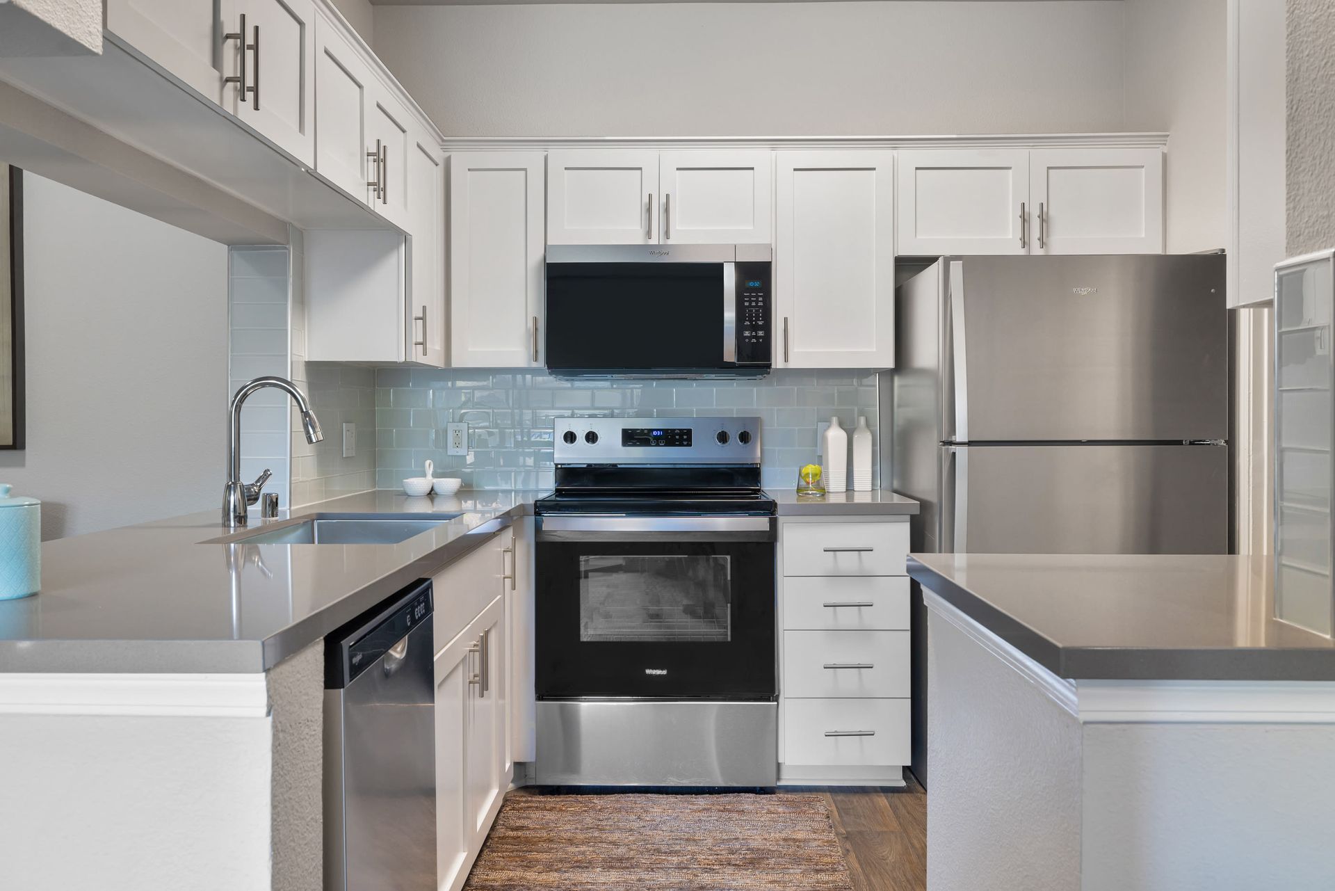 Modern kitchen with white cabinets, stainless steel refrigerator, oven, microwave, and sink at Alize Apartment Homes in Aliso Viejo, CA.