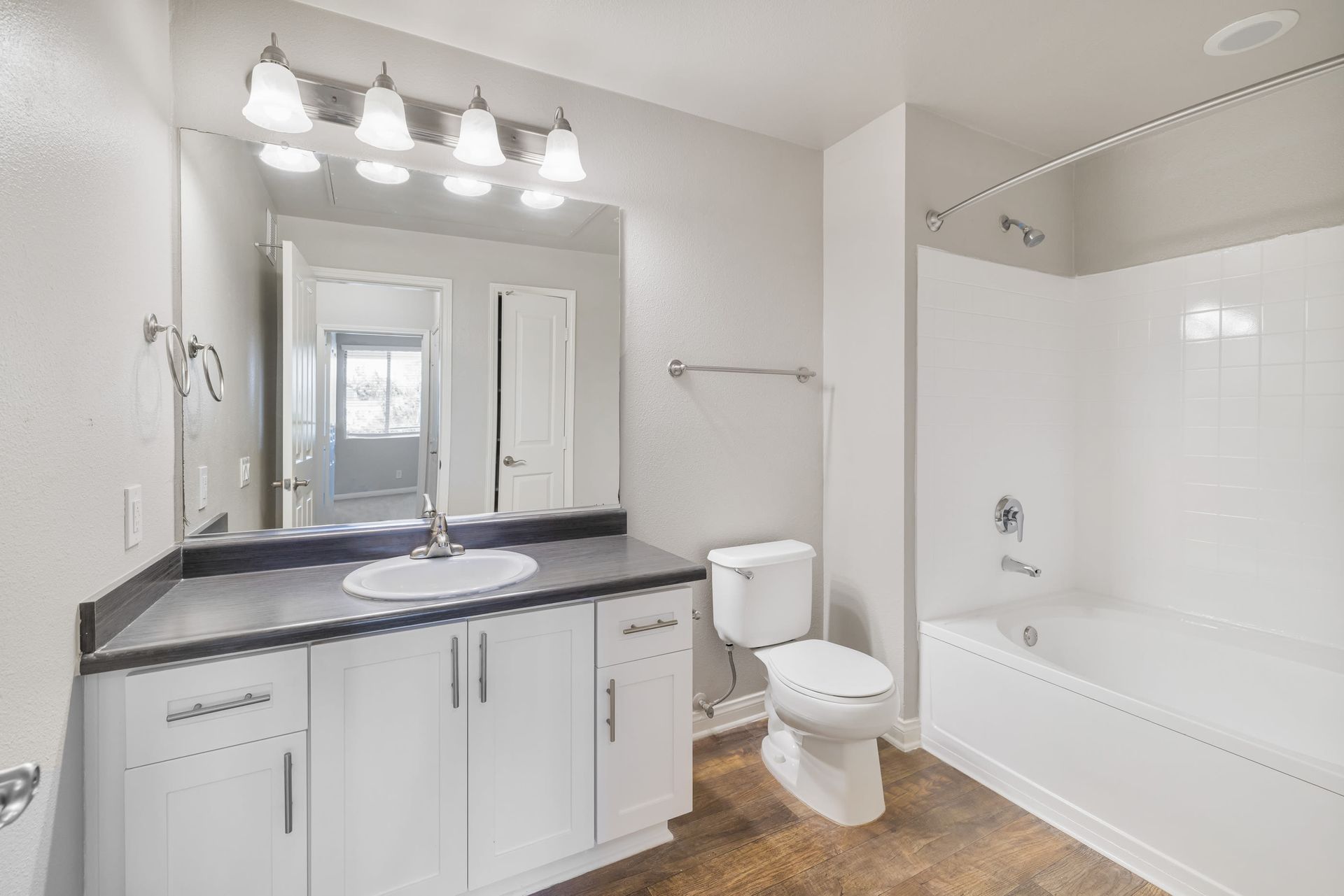 Bathroom with white vanity, dark countertop, large mirror, toilet, and a bathtub/shower at Alize Apartment Homes in Aliso Viejo, CA.