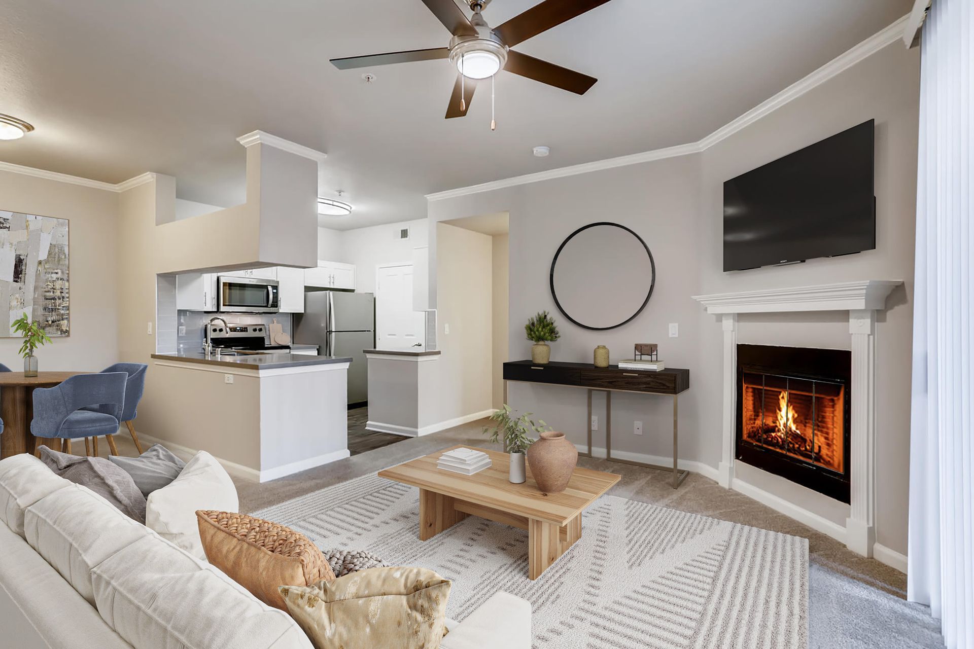 Open living room with fireplace, wall-mounted TV, sofa, and a visible kitchen in the background at Alize Apartment Homes in Aliso Viejo, CA.