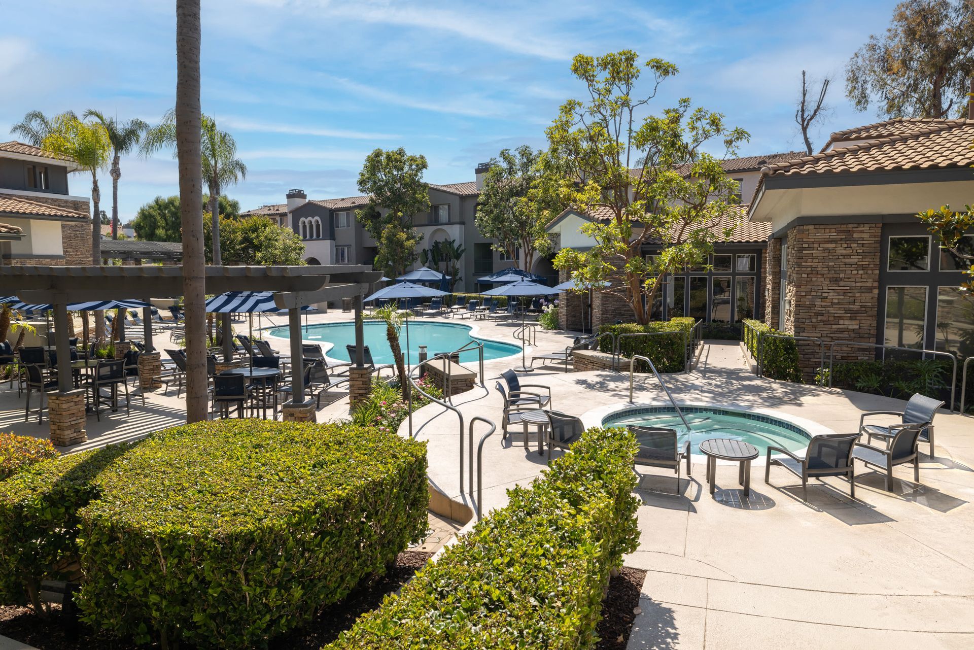 Outdoor apartment community pool area with lounge chairs, umbrellas, and surrounding landscaping at Alize Apartment Homes in Aliso Viejo, CA.