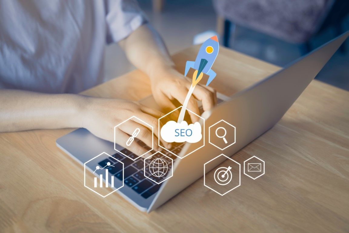 Person typing on a laptop with overlaid SEO icons and a rocket launching from an SEO cloud.