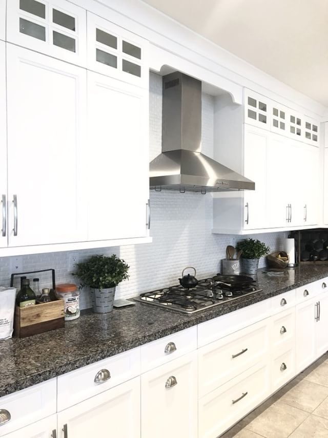 White kitchen cabinets with stainless steel range hood above a stovetop, granite countertop.
