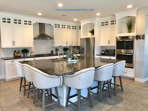 White kitchen with granite island and white cabinets. Island has seating, stainless steel appliances.