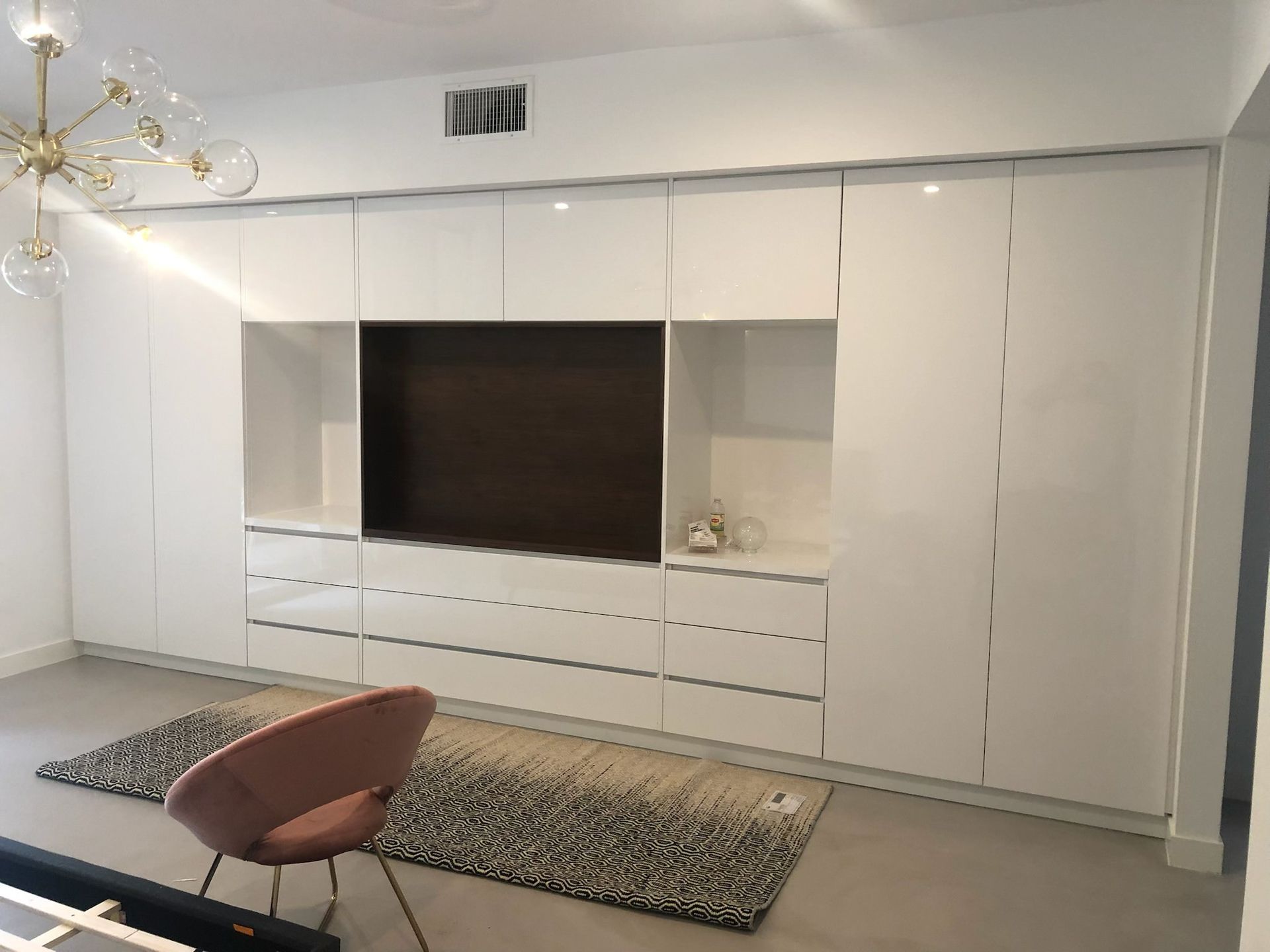 White built-in wall unit with a dark TV area. A pink chair and rug sit in front.