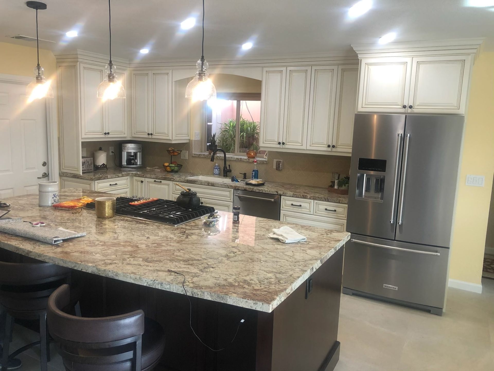 Kitchen with granite countertops, stainless steel refrigerator, white cabinets, and island with seating.