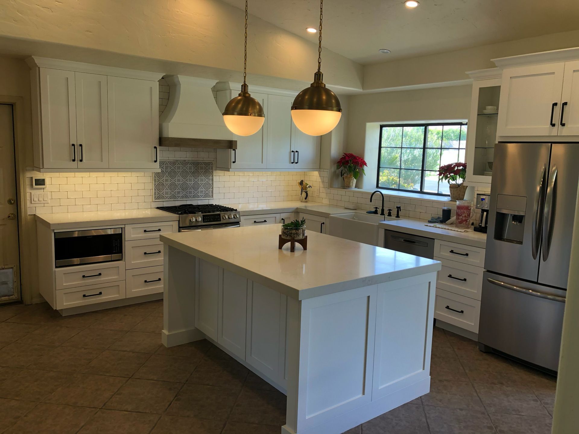 White kitchen with island, stainless steel appliances, and pendant lights.