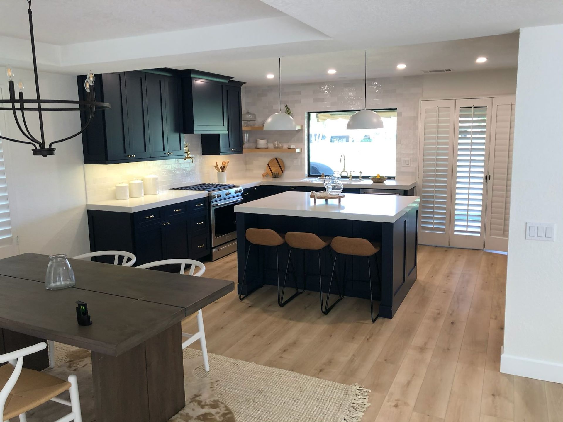 Modern kitchen with navy cabinets, white countertops, island with barstools, and light wood flooring.