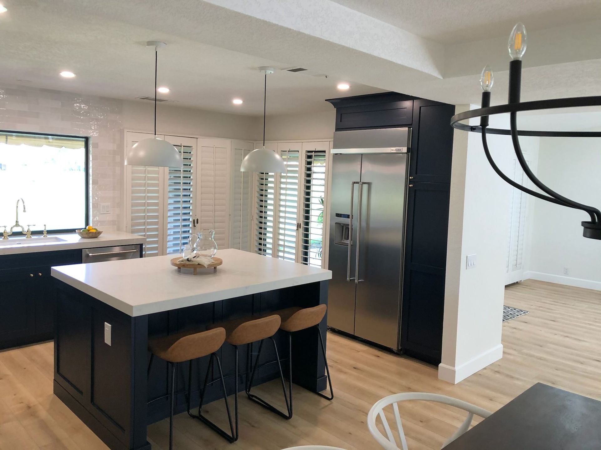 Modern kitchen with blue island and cabinets, white countertops, stainless steel refrigerator, light wood floors.