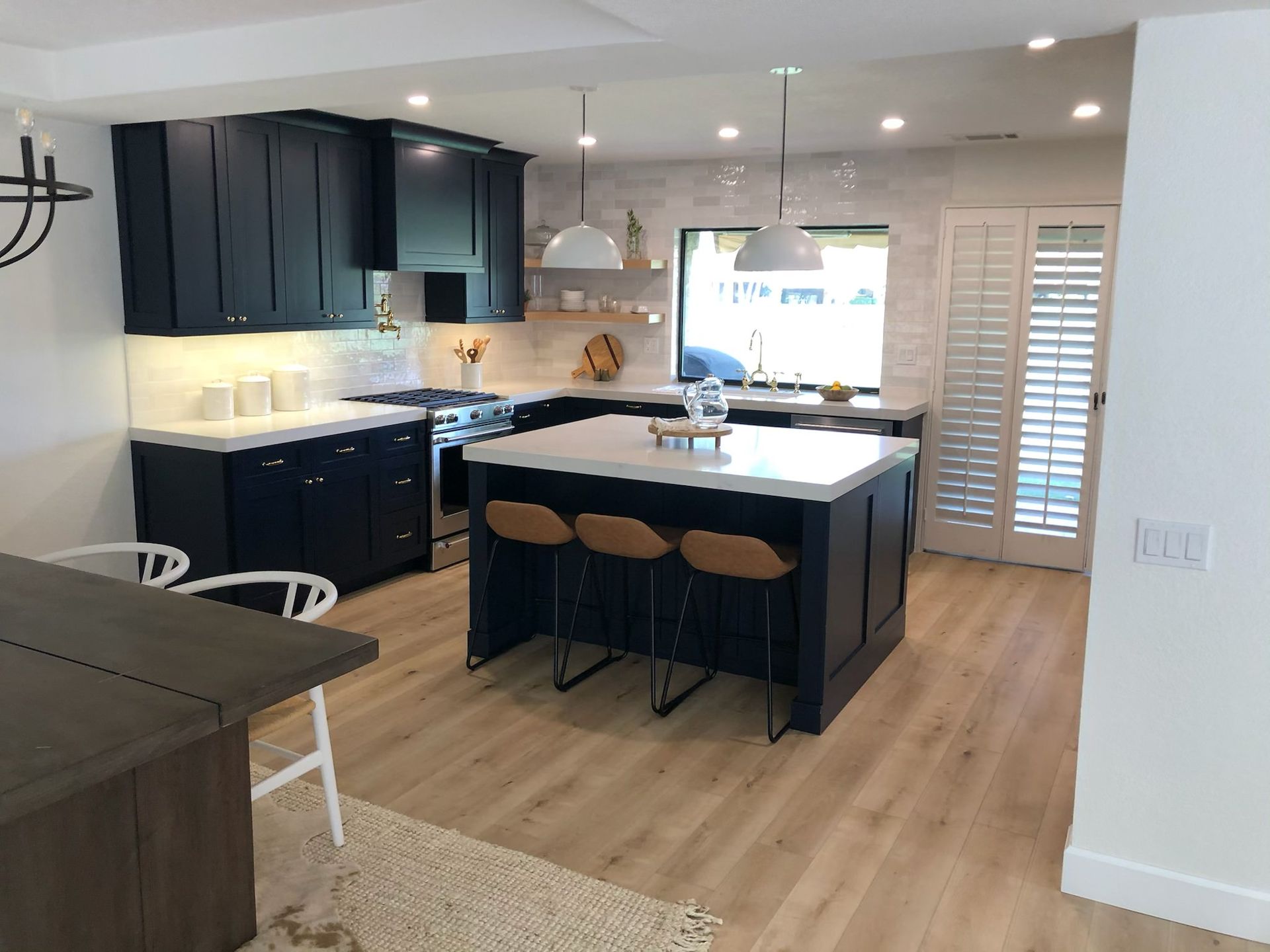 Modern kitchen with navy cabinets, white countertops, and wood flooring. Island with stools, window with shutters.