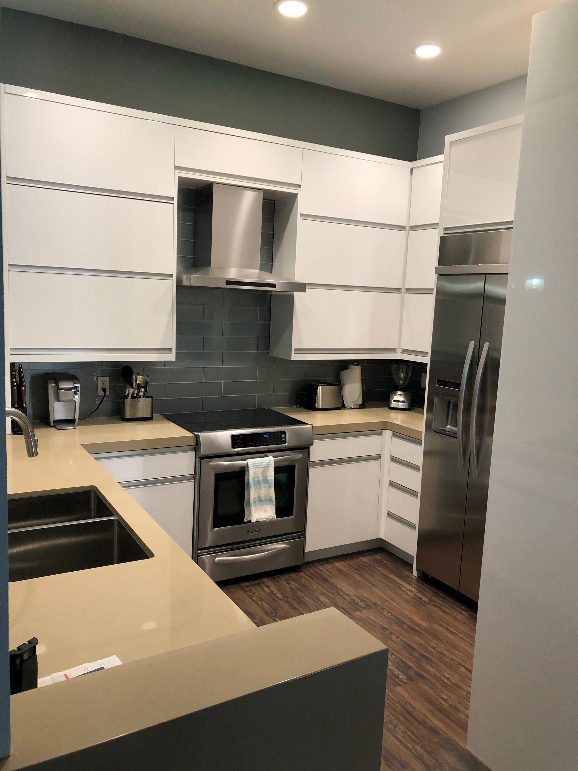 Modern white kitchen with stainless steel appliances, light countertops, and dark wood floors.