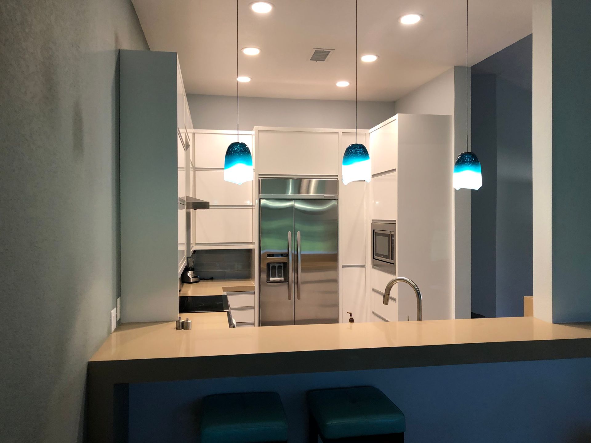 Modern kitchen with white cabinetry, stainless steel appliances, and turquoise pendant lights.