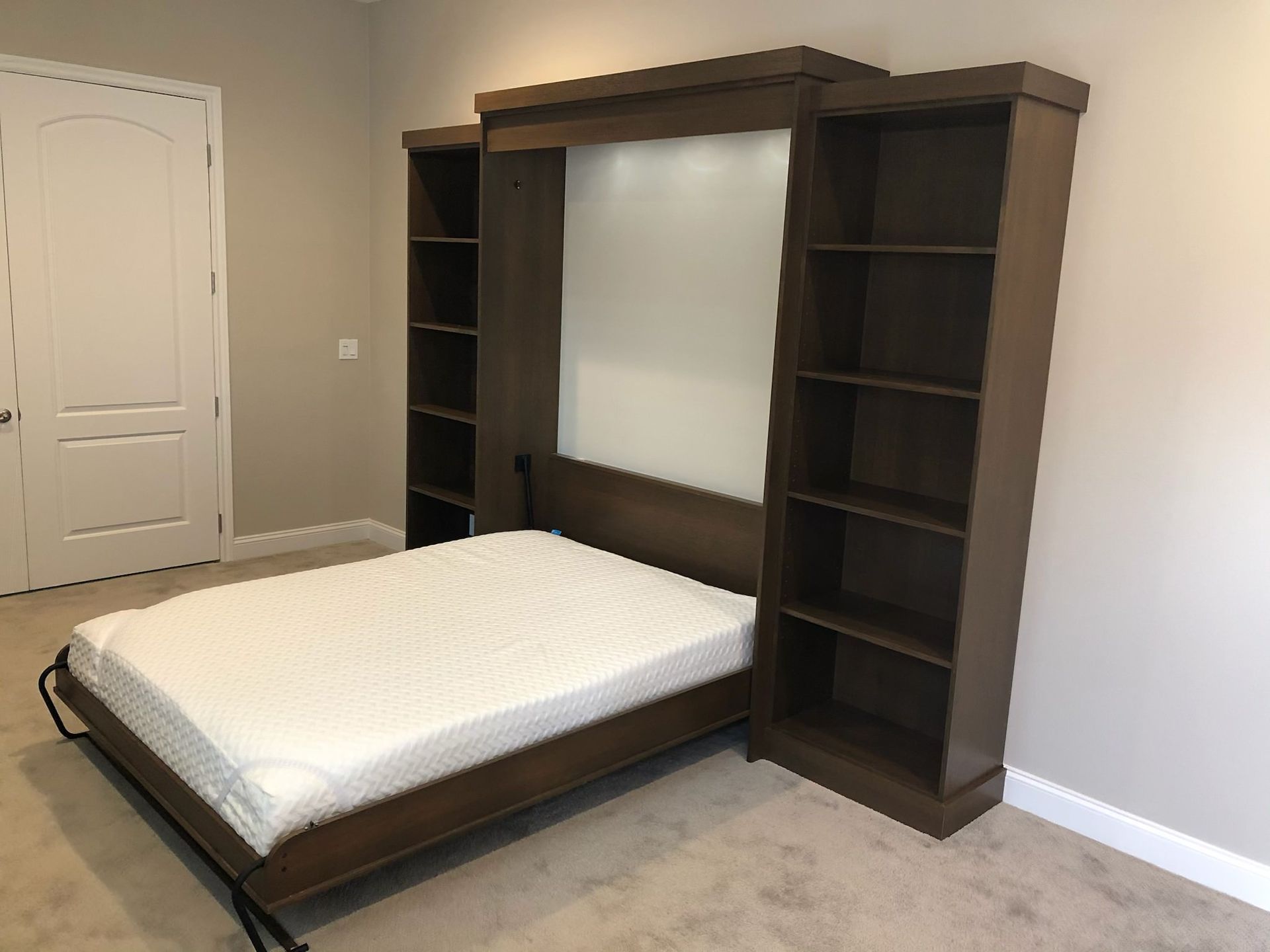 A brown wall-mounted bed with bookshelves on either side, against a beige wall, a door is on the left.