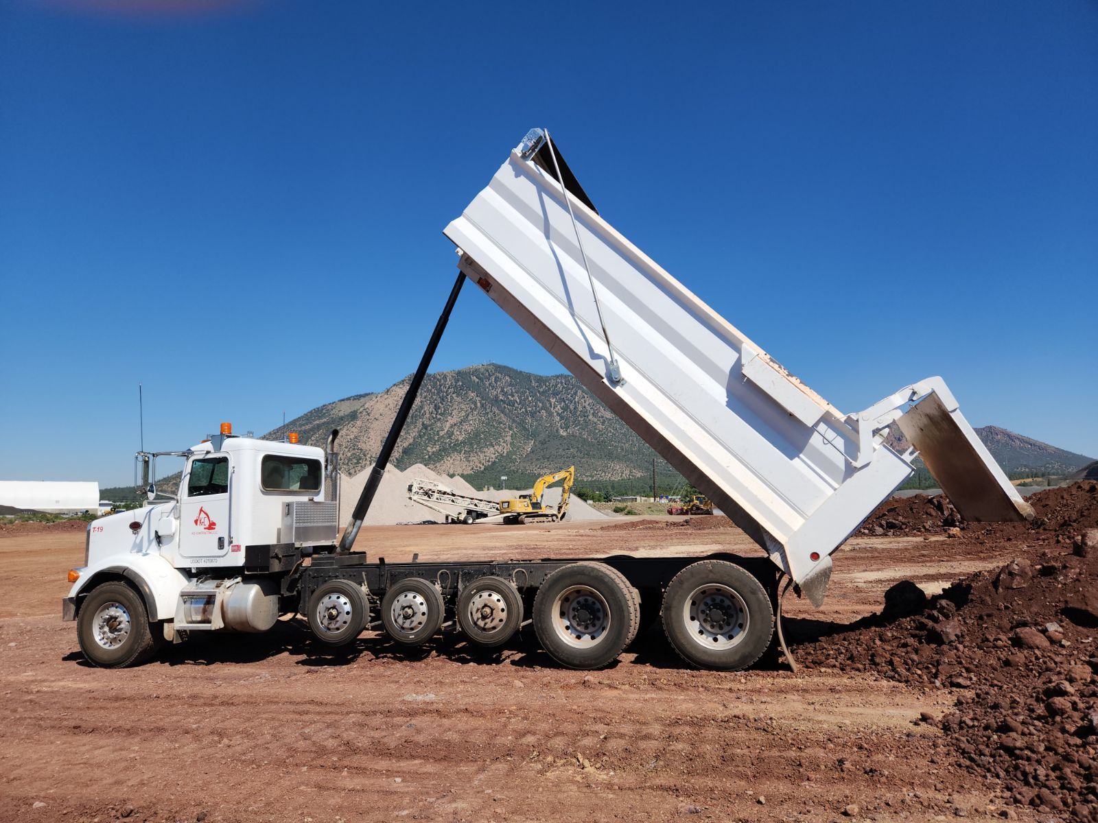 A dump truck is sitting in a dirt field with its bed open.