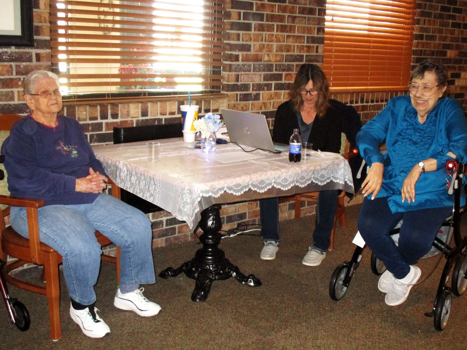 Three elderly women are sitting around a table with a laptop on it
