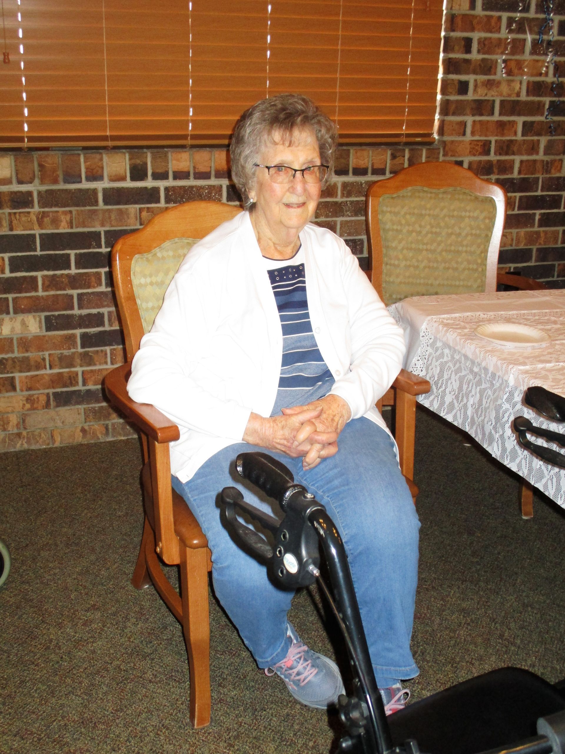 An elderly woman is sitting in a chair next to a table