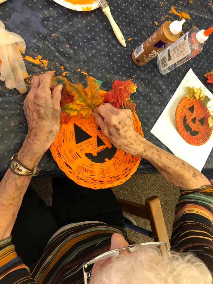 An woman is sitting at a table decorating a pumpkin