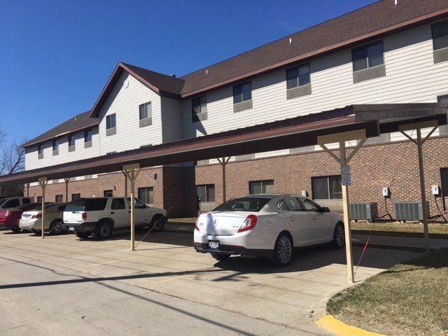 A white car is parked under a canopy in front of a building