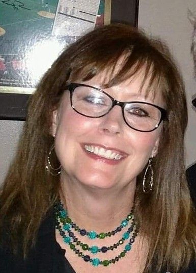 A woman wearing glasses and a necklace is smiling.