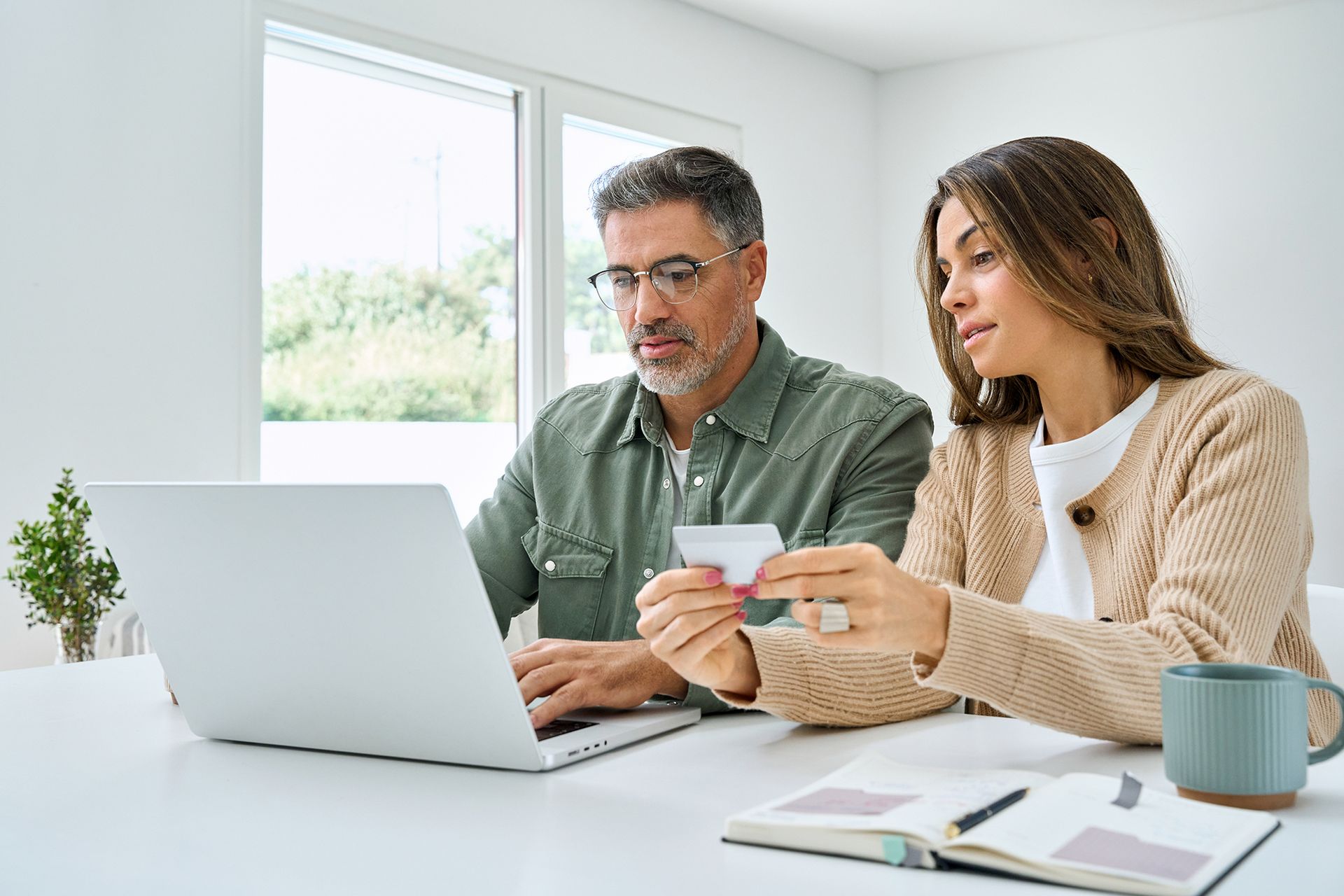 A man and a woman are sitting at a table looking at a laptop.