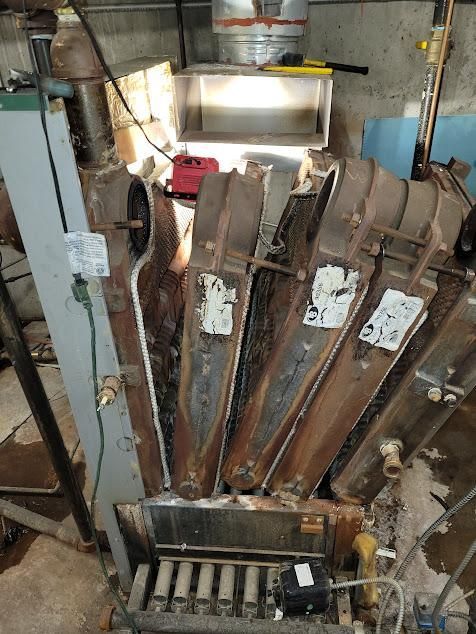 Old, rusty boiler with multiple angled chambers. Indoor setting.