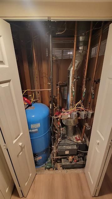 Blue water tank and furnace inside a closet, with copper pipes and wiring.