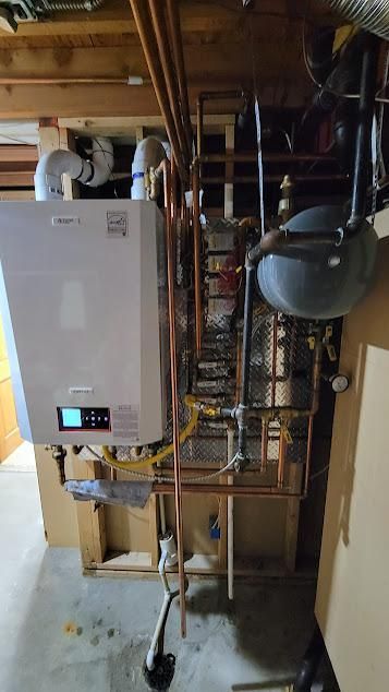 A white wall-mounted boiler with copper pipes in a basement setting.