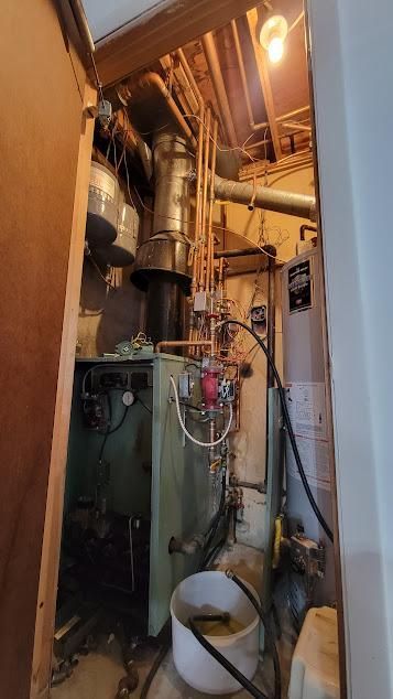 Old furnace and plumbing in a basement. Pipes are copper. The setting is industrial.