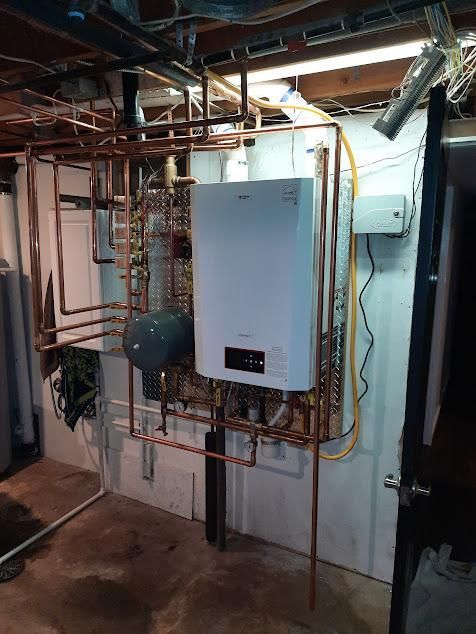 Copper pipes and a white boiler on a basement wall.