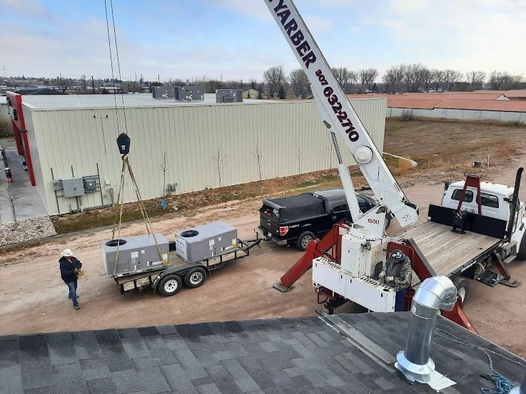 Crane lifting equipment onto a building roof; worker nearby.