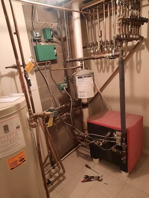 Plumbing system with copper pipes, a red boiler, and multiple green control boxes in a basement.