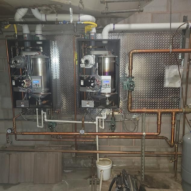 Two modern gas boilers with copper pipes in a basement setting.