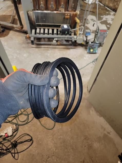 A gloved hand holds a stack of black rubber rings in a workshop setting, with industrial equipment in the background.