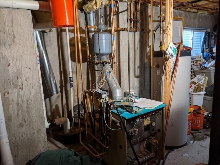 A basement with a boiler, hot water tank, and copper pipes.