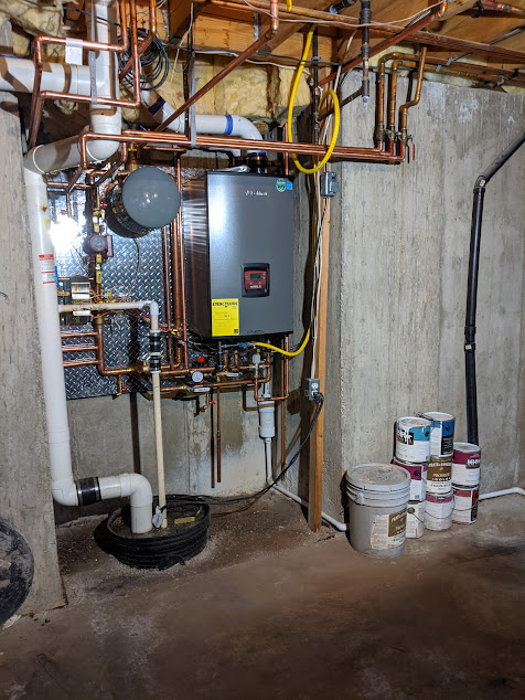 Plumbing and heating system in a basement; copper pipes, gray boiler, sump pump. Paint cans on floor.
