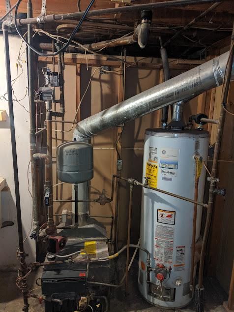 Water heater and furnace in a basement, with pipes, ductwork, and electrical components visible.