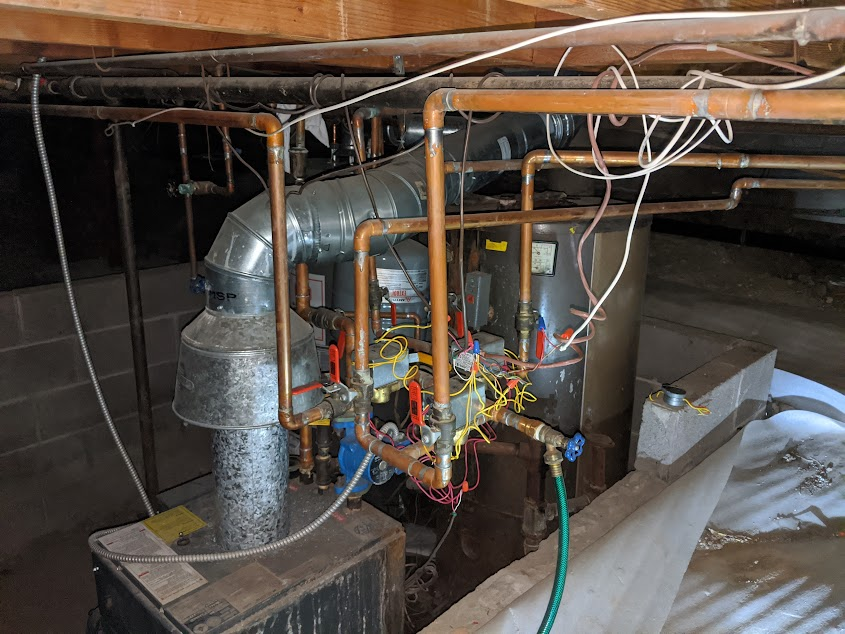 Basement boiler system with copper pipes and electrical wiring, silver ductwork, and green hose.
