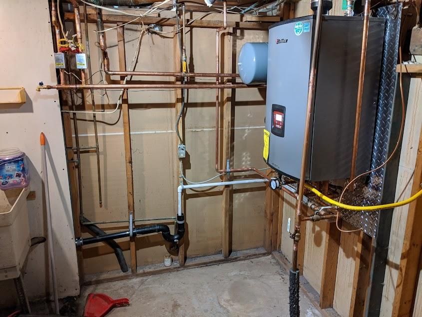 Basement with water heater, copper pipes, and exposed framing. Gray unit on right.