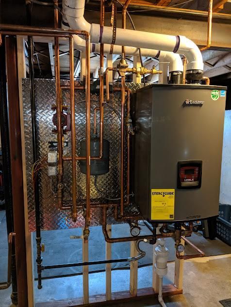 Copper pipes and boiler in a basement, mounted on wood framing.