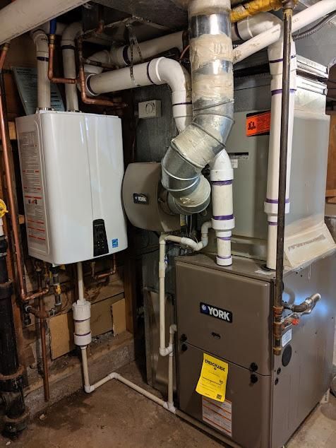 A gas furnace and water heater installed in a basement with white pipes and copper tubing.