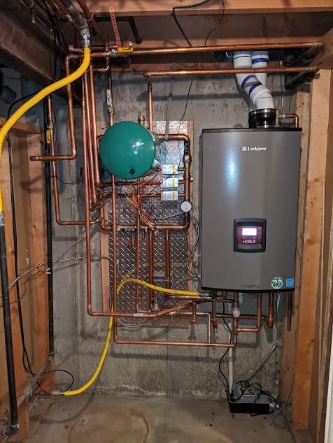 Gas boiler with copper pipes and green pressure tank in a basement setting.