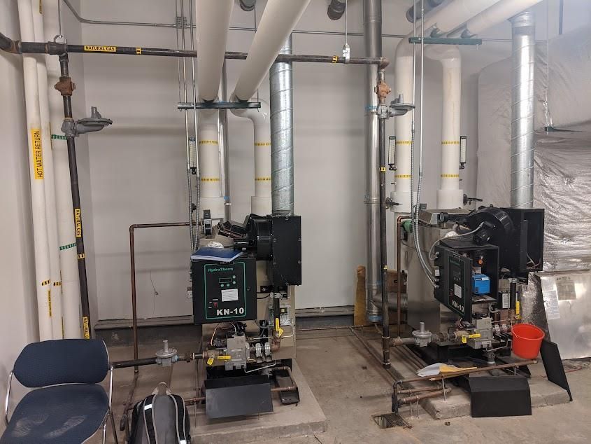 Two industrial boilers with piping in a utility room.