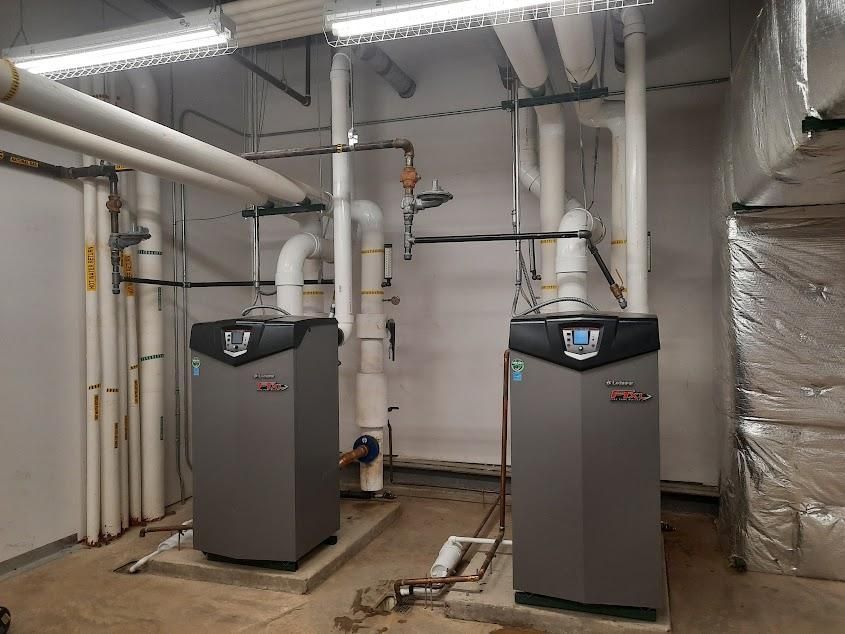 Two large gray heating units with connected pipes in a utility room.