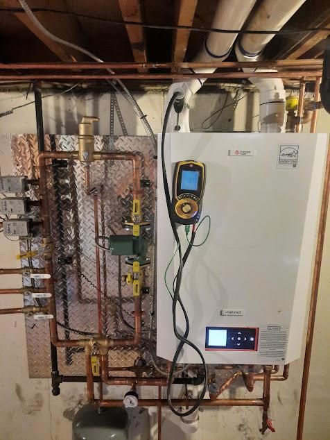 A wall-mounted white boiler with attached copper pipes, gauges, and control panel in a utility room.