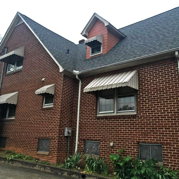 A brick house with a roof and awnings on the windows