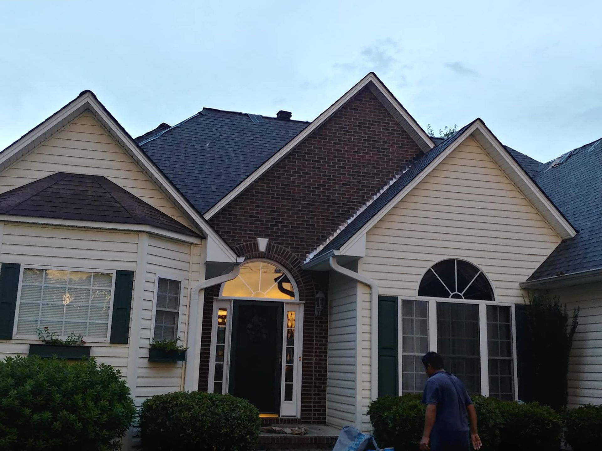 A man standing in front of a white house with a brick roof