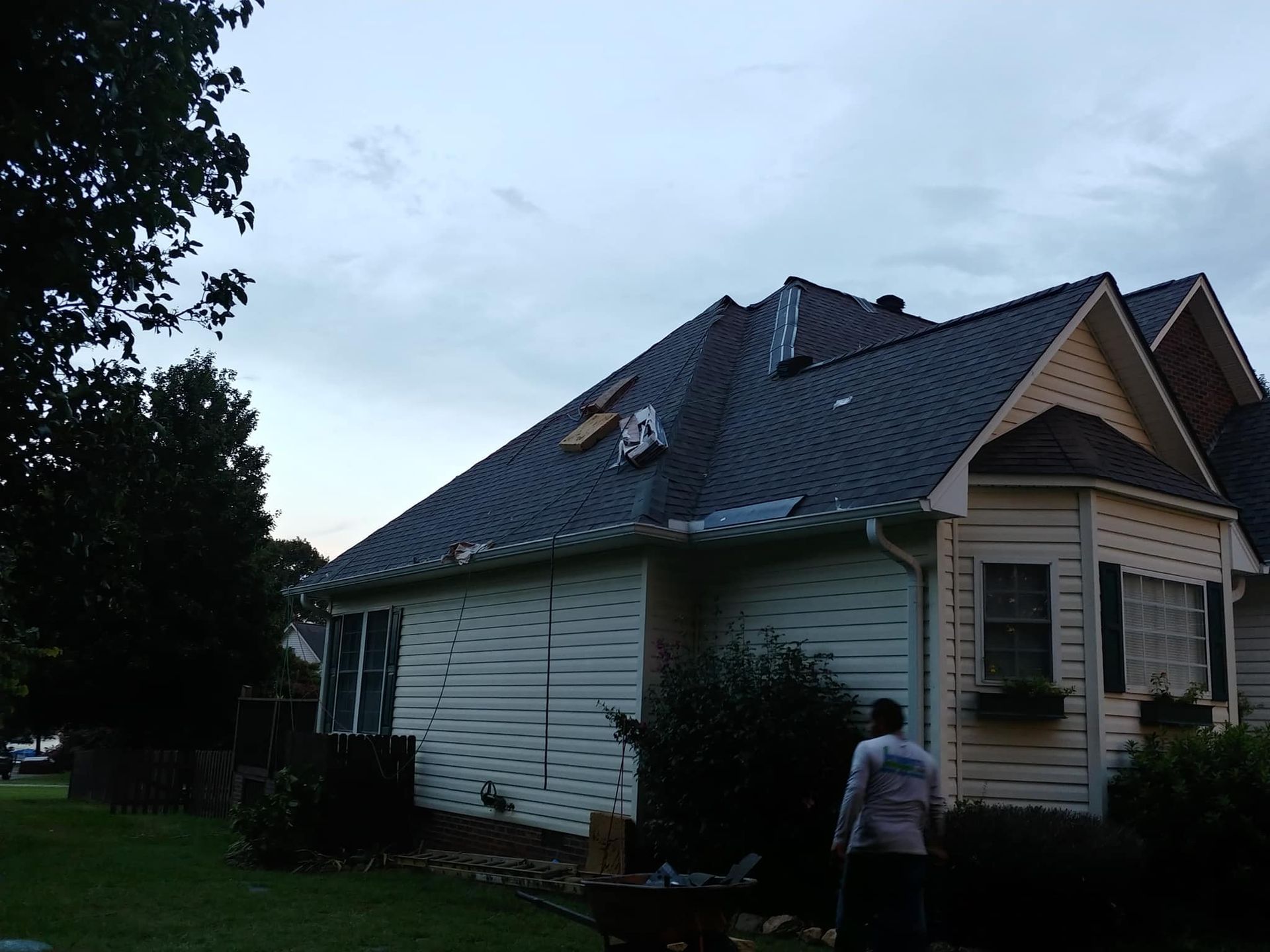 A man is standing in front of a house with a roof that is missing shingles